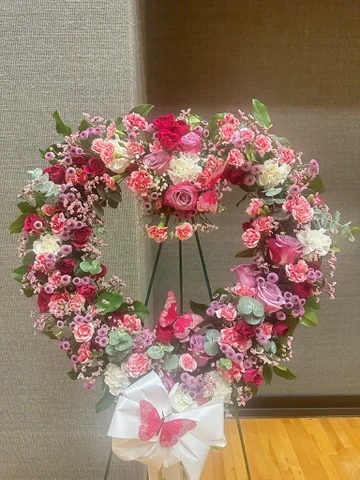 Heart-shaped wreath on an easel, made from pink and cream roses with butterfly detail.
